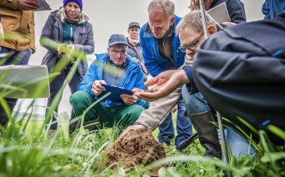 Eine Person erklärt Interessierten etwas auf einem Feld